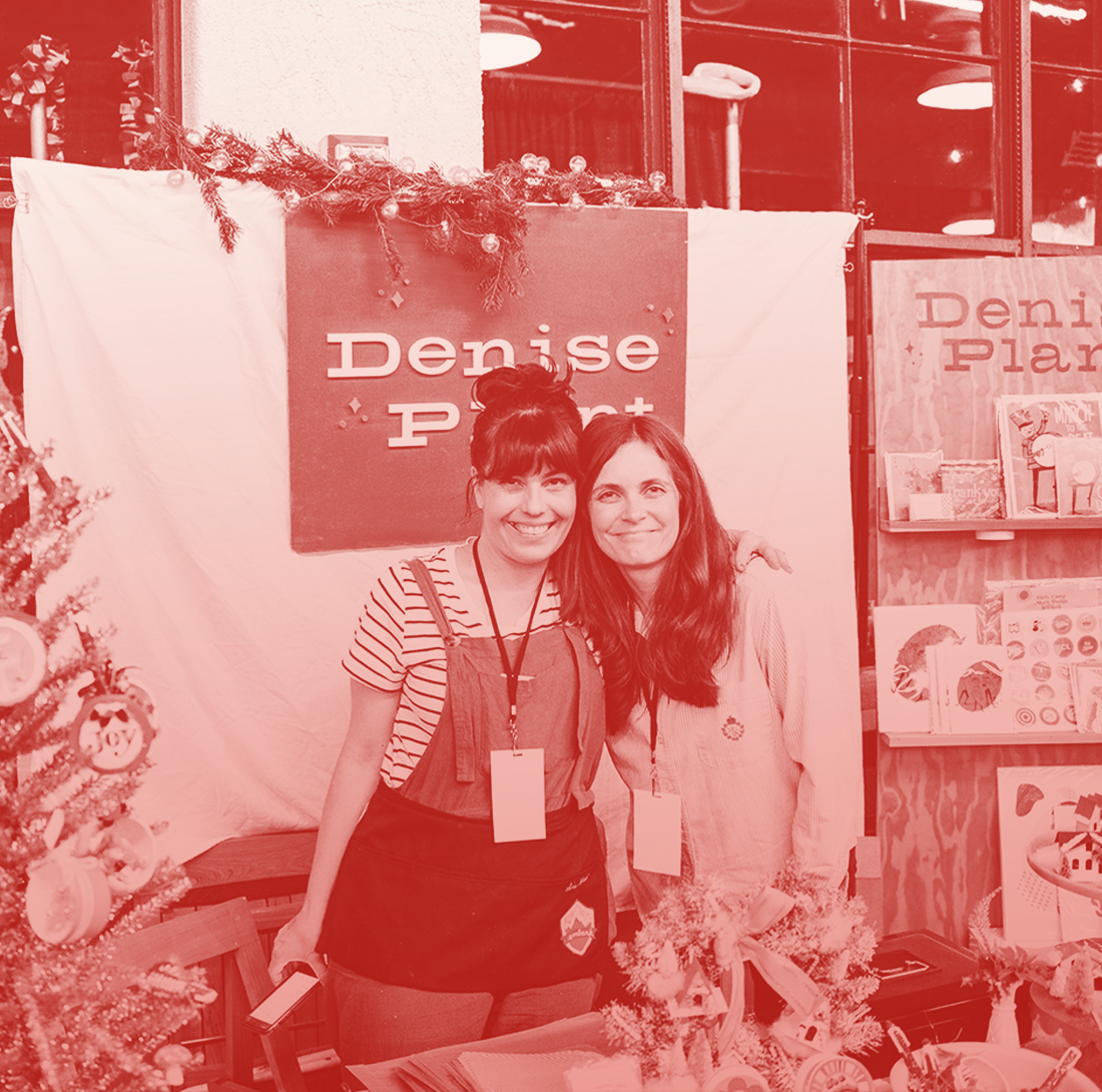 2 artisan exhibitors posing in front of their booth at the Holiday Market.